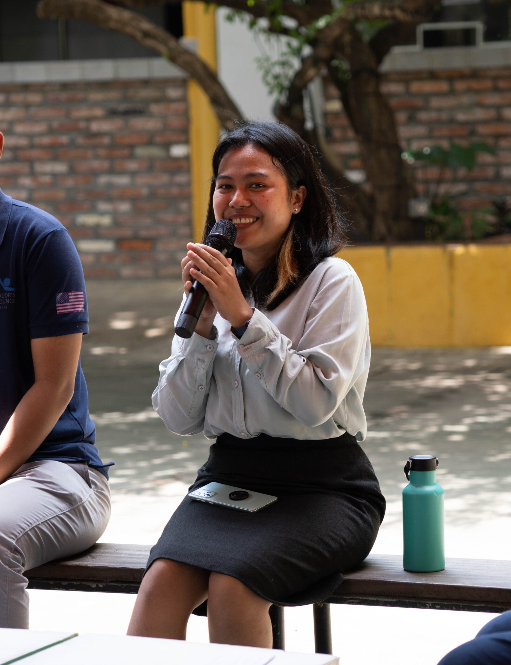 A young women smiles and speaks into a microphone at the Local Conference of Youth (LCOY) in Cambodia.