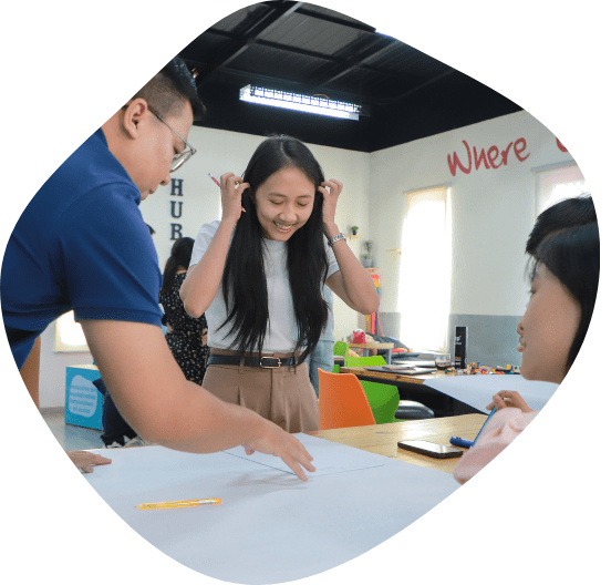 Three entrepreneurs stand over a flipchart paper in discussion during a bootcamp for the SAAMBAT Digital Agriculture Accelerator.