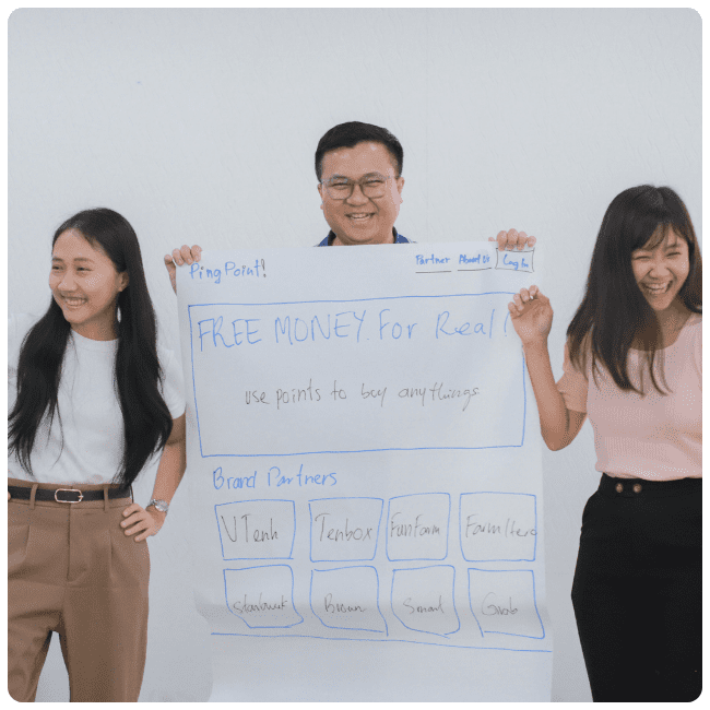 One man and two women stand next to each other holding up a flipchart paper and laughing.