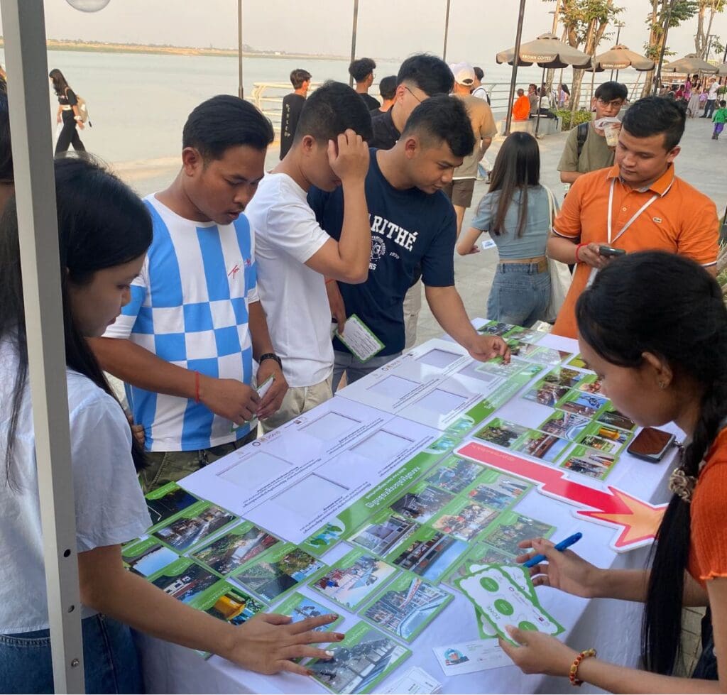 A small group of people stand around a table at the Koh Norea riverside in Phnom Penh moving around cards illustrated with urban features.
