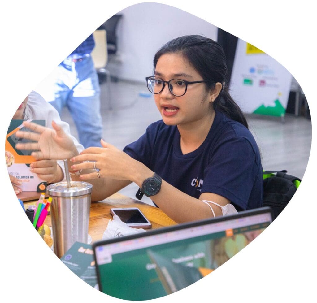 A young woman sits at a table speaking with her hands during a workshop of Impact Hub Phnom Penh's SmartSpark+ Incubation Program.