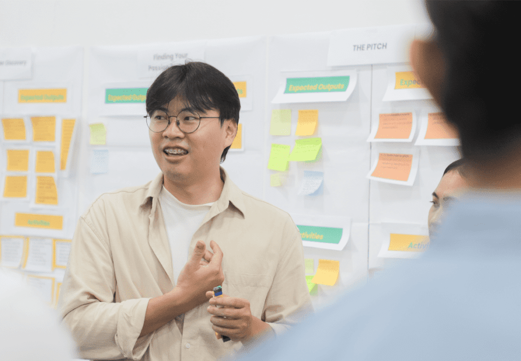 A zoomed in photo of an Impact Hub Phnom Penh staff member as he leads a workshop. Behind him are colorful notes and flipchart on the wall.