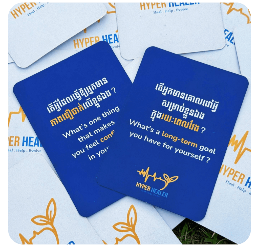 A collection of blue and white cards, featuring reflective questions in English and Khmer. Prominent blue cards ask about personal comfort and long-term goals, branded "Hyper Healer." The tone is introspective and motivational.