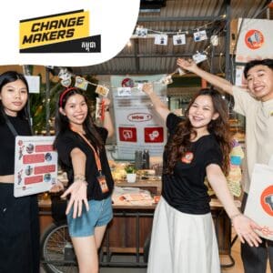 A group of four smiling people at a booth display festival atmosphere with "Changemakers" banner. They're holding a string of photos, creating a lively and engaging scene.