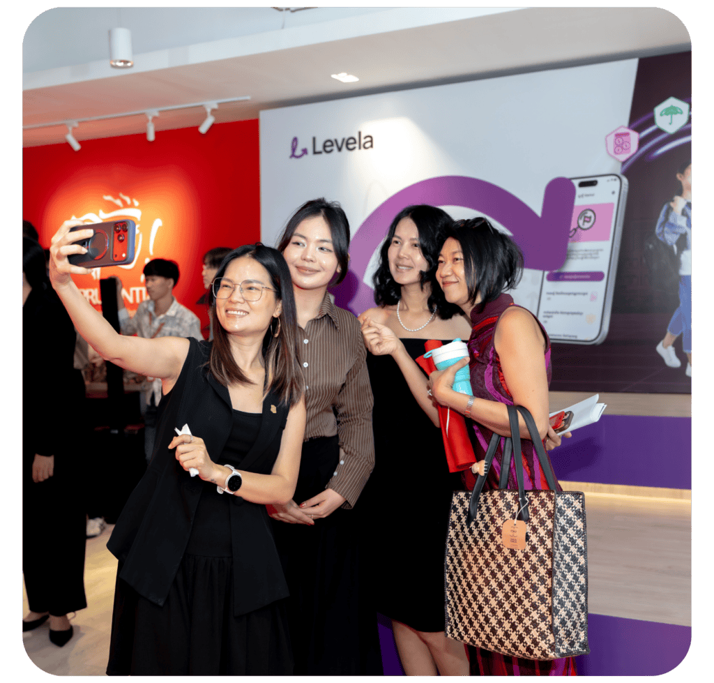 Four women taking a selfie together at an event, with a colorful background featuring a logo and promotional materials.